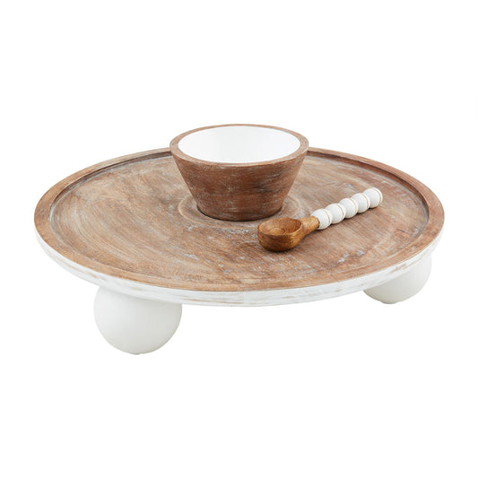 The Pedestal Chip N Dip is a round mango wood tray with three white legs, featuring a small wooden bowl and a scoop with a white handle. Available size: One size.
