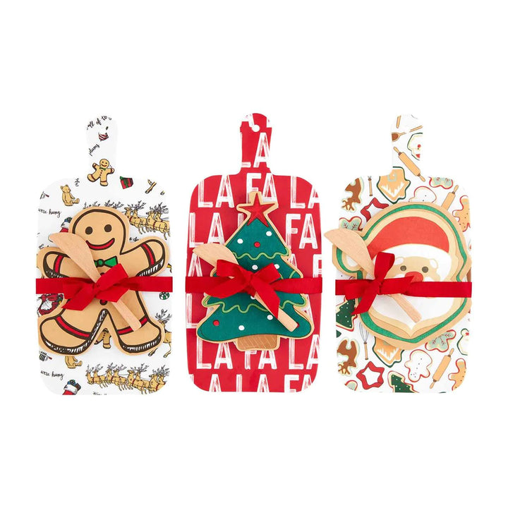 Christmas Melamine Board and Napkin Set with three rectangular shatterproof melamine paddle boards in gingerbread man, tree, and Santa patterns, each with a red ribbon and wooden spreader.
