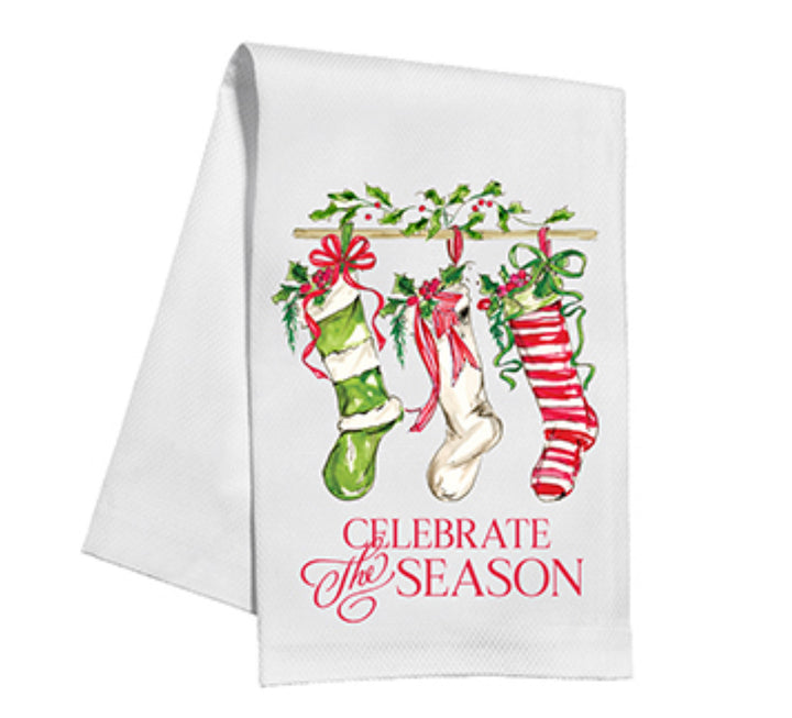 Holiday Handpainted Kitchen Towels: festive white towel with three Christmas stockings on a wooden rod, holly, and bows. "Celebrate the Season" in red cursive at the bottom. 100% cotton, machine-washable. Sizes available: Standard (28x18 inches).
