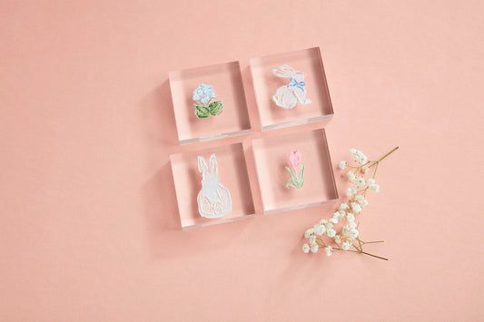 The Spring Acrylic Block set includes four clear blocks showcasing hand-painted acrylic art: a vibrant flower, a rabbit with a blue bow, another rabbit, and a tulip. Sizes available: Standard.