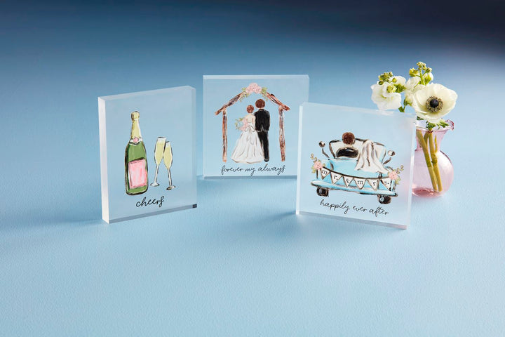 The Acrylic Wedding Plaque showcases hand-painted wedding illustrations like a champagne bottle, a couple under an arch, and "happily ever after" on a car. Available sizes: 8"x10", 12"x15", 16"x20".