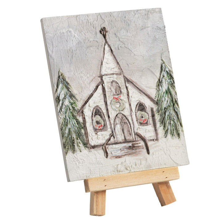 Square Holiday Farmhouse Art plaque featuring a painted winter church scene with wreaths and pine trees.