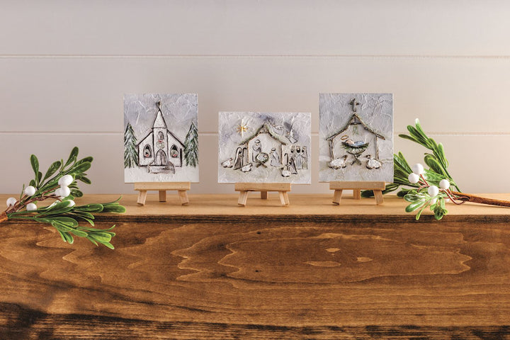 Three Holiday Farmhouse Art Plaques on mini wooden easels with rectangular church, nativity, and angel designs.