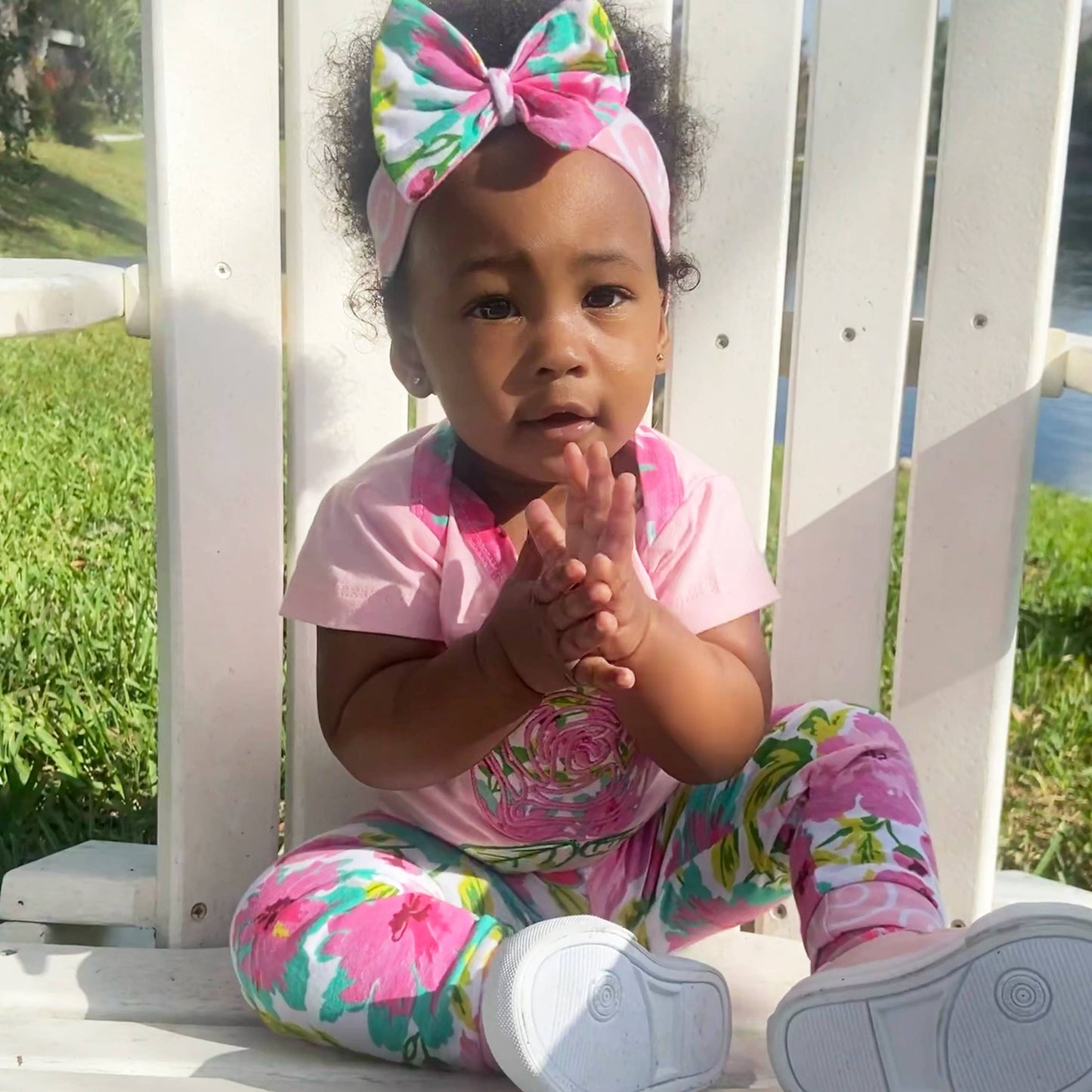 Baby modeling the set with white sneakers on. Sitting on a white wooden chair outside whilst clapping her hands.