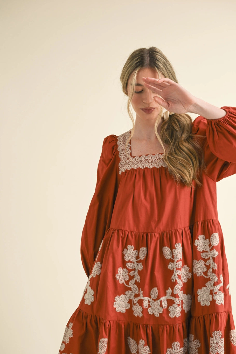 Rust-colored midi dress with square neckline, long sleeves, and white floral embroidery on bodice and tiered skirt. Available in various sizes.