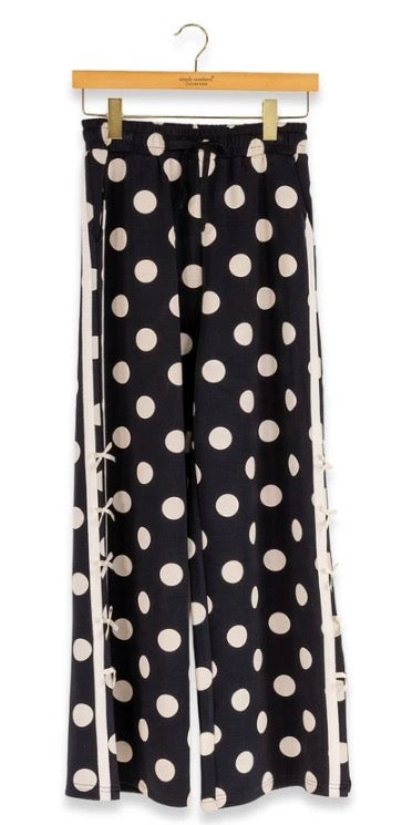 Black wide-leg lounge pants with large white polka dots, white side stripes, and small decorative bows along the sides. Available in sizes S, M, L, XL.
