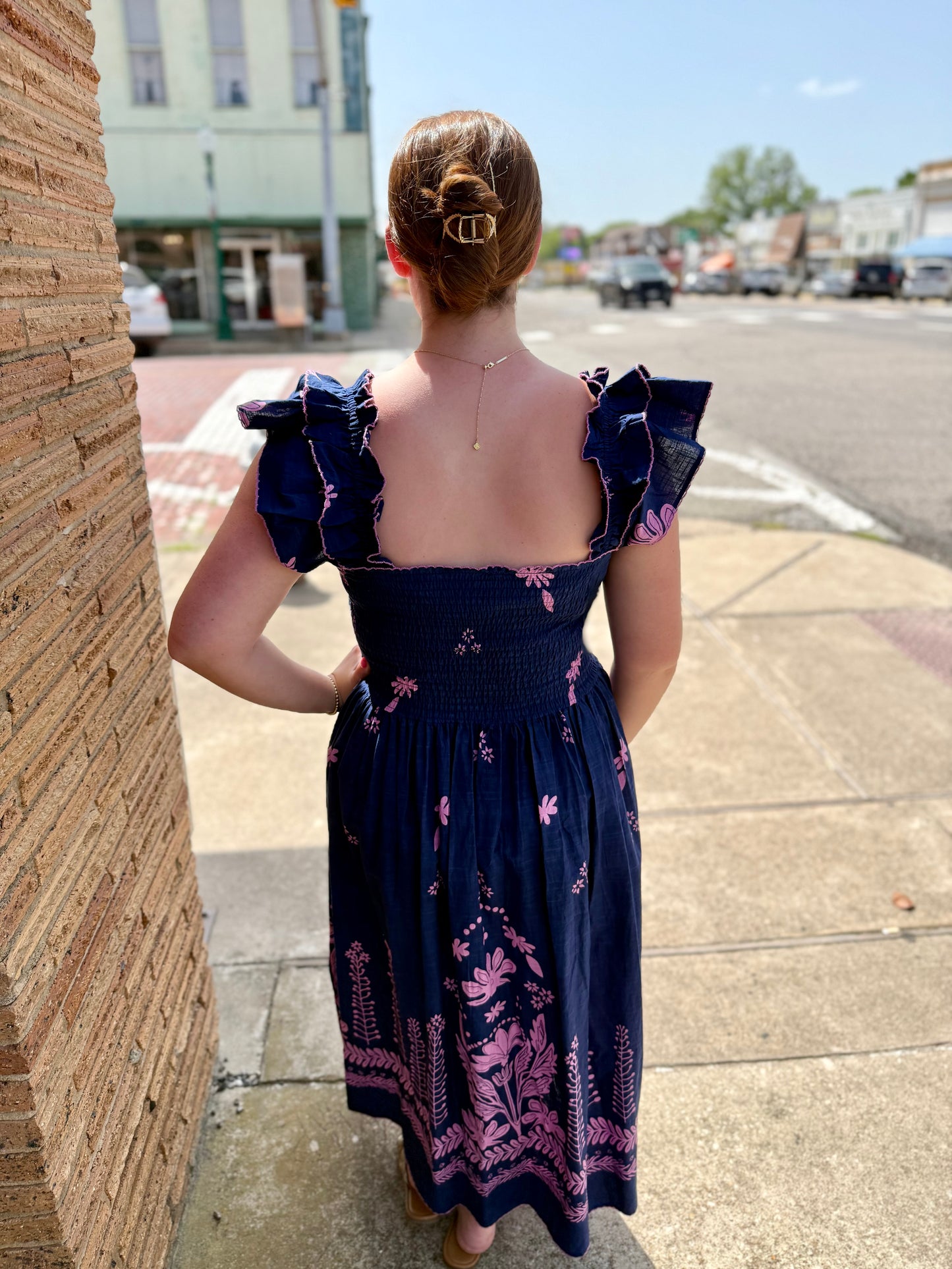 Navy Smocked Border Dress with pink floral patterns and ruffled sleeves. Available in sizes XS-XL.
