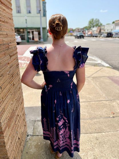 Navy Smocked Border Dress with pink floral patterns and ruffled sleeves. Available in sizes XS-XL.