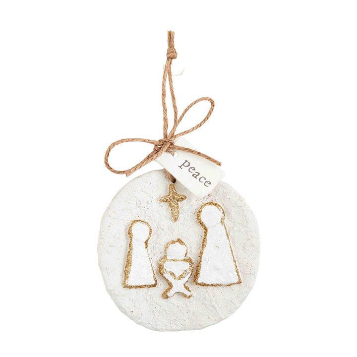Circular white glitter papier-mâché ornament featuring a gold-glittered nativity scene and a “peace” hanging tag.