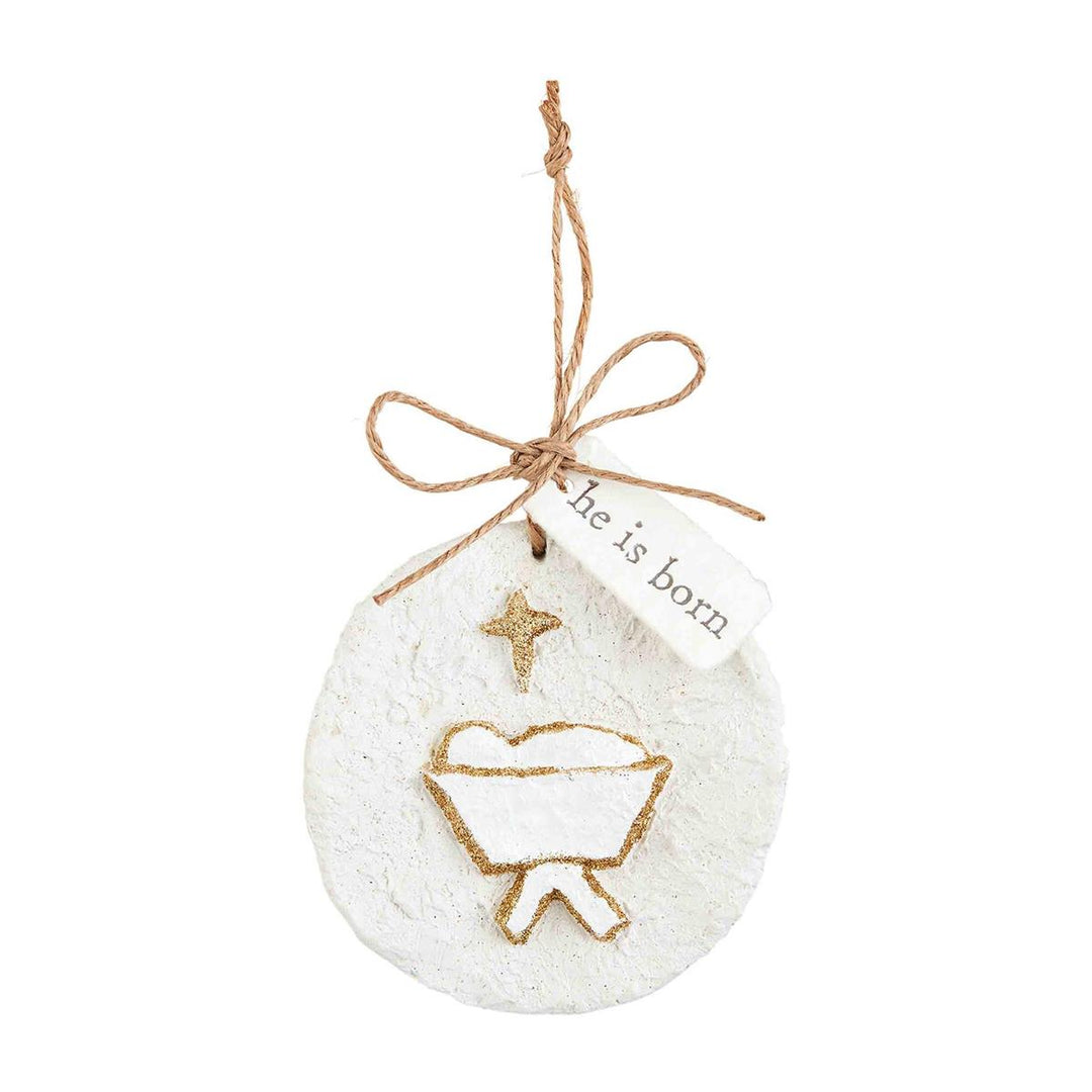 Round, textured white glitter papier-mâché ornaments with gold glitter manger, star design, “he is born” tag, and twine hanger.