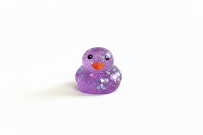 Glitter Squishy Duck: small purple rubber duck with orange beak, black eyes, and glitter accents. Available in small size.