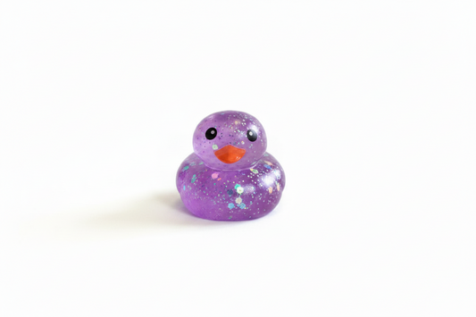 Glitter Squishy Duck: small purple rubber duck with orange beak, black eyes, and glitter accents. Available in small size.
