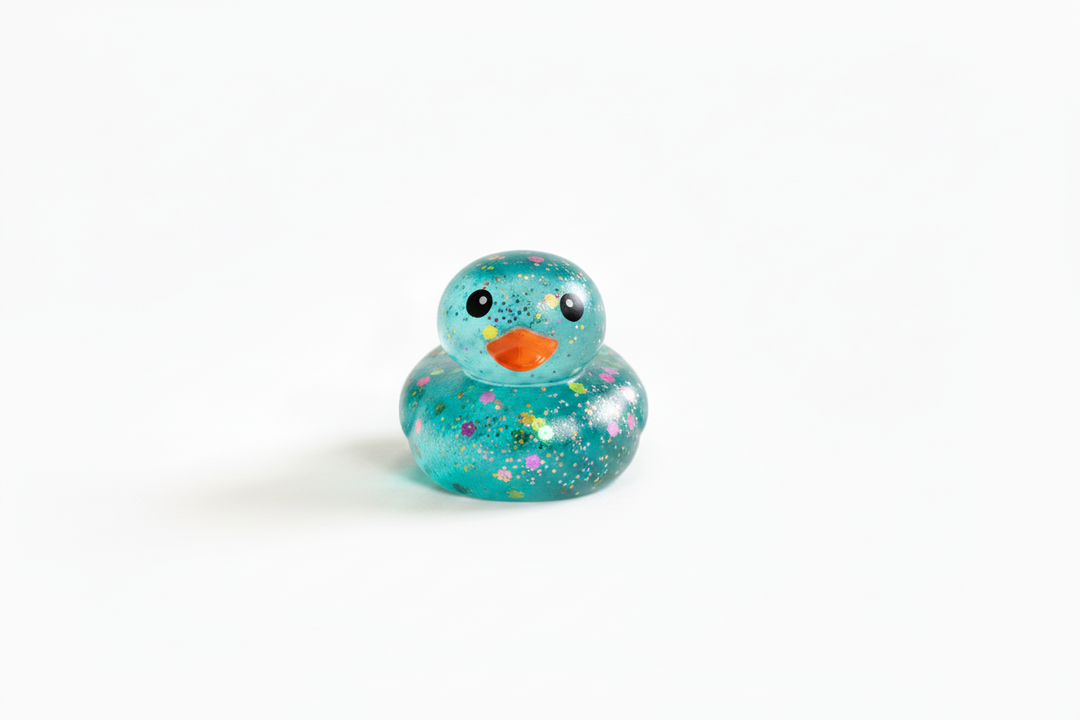 Teal Glitter Squishy Duck with black eyes, orange beak, colorful glitter, and flower patterns. Available in multiple sizes.