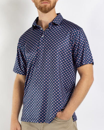 Men’s Americana Performance Polo: navy blue short-sleeve shirt with a red and white geometric pattern. Available in sizes S–XXL.