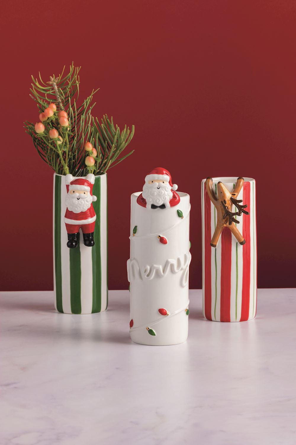 Three hanging ceramic cylindrical vases featuring Santa and reindeer designs with red or green vertical stripes or Christmas lights.