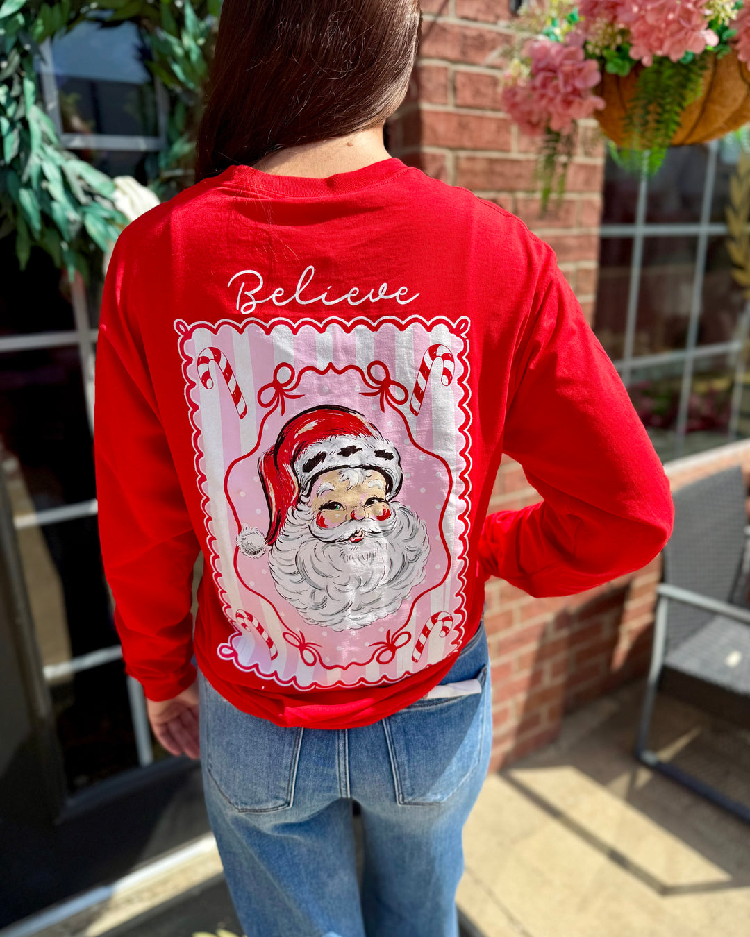 Jolly Santa Scalloped Long Sleeve: festive red holiday top with a Santa Claus illustration and “Believe” on the back; available in sizes S–XXL.