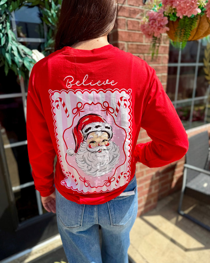 Jolly Santa Scalloped Long Sleeve: festive red holiday top with a Santa Claus illustration and “Believe” on the back; available in sizes S–XXL.