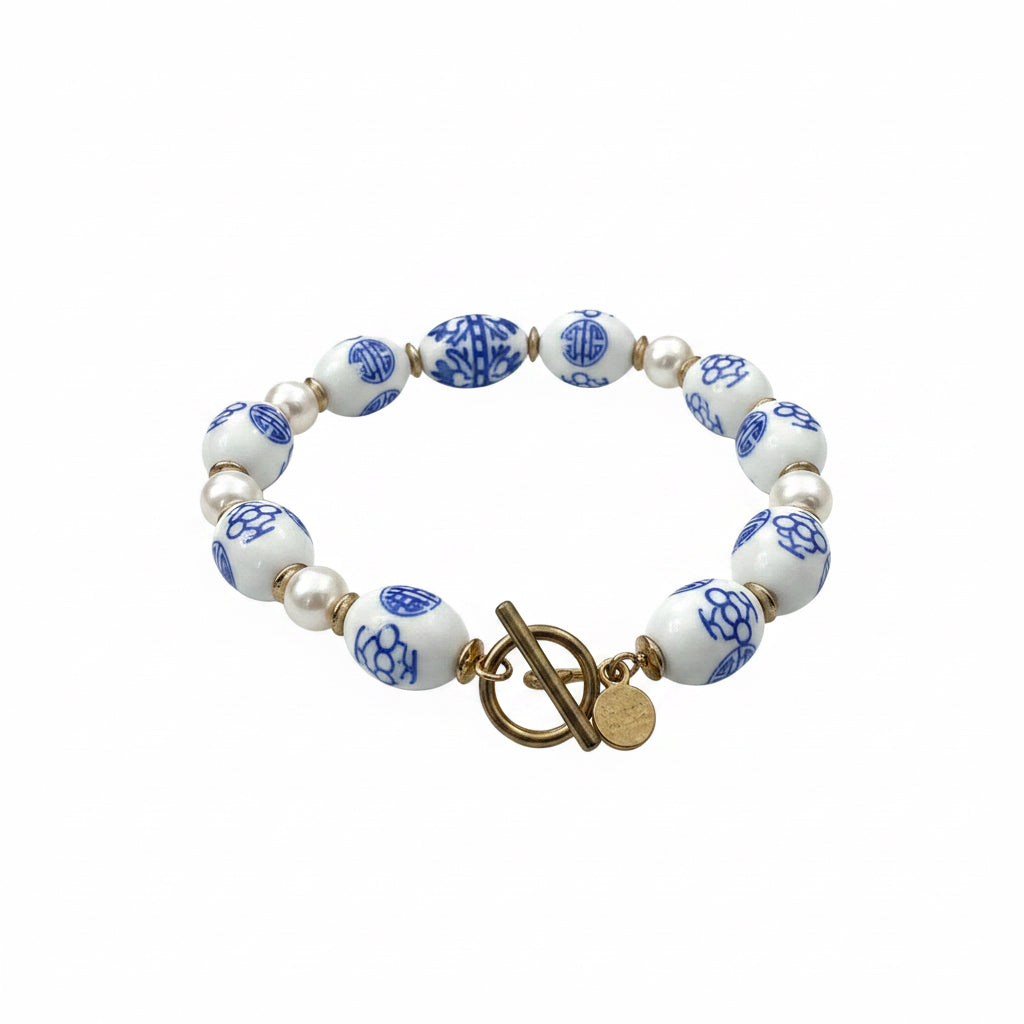 Chinoiserie Pearl Stretch Bracelet with alternating white and blue ceramic beads, gold beads, a gold toggle clasp, and small round gold charm. Available in multiple sizes.