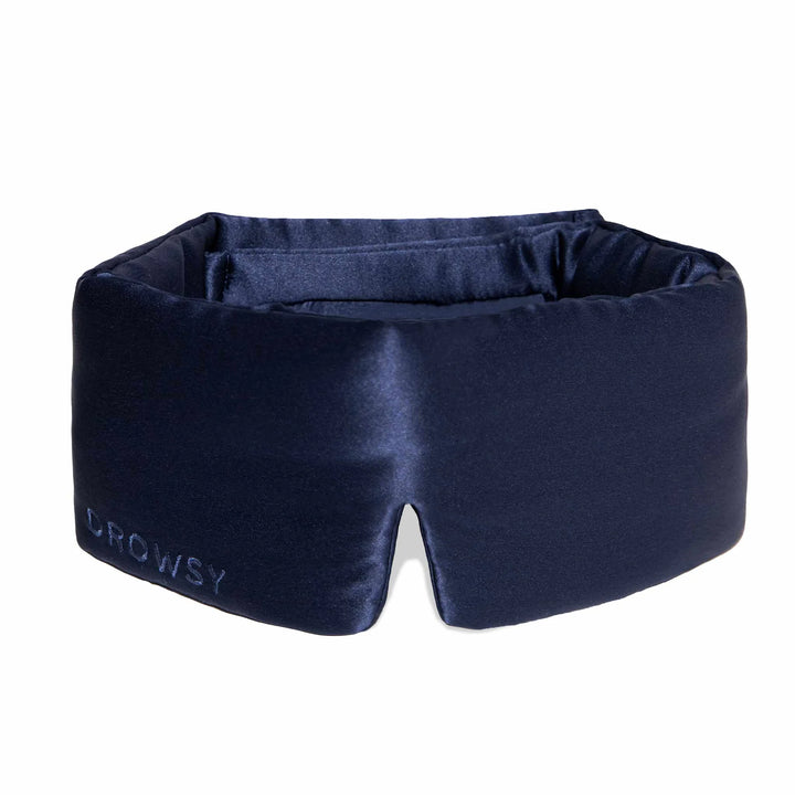 Navy blue satin blackout sleep mask with thick padding, notched center, and "DROWSY" embroidered. Sizes: standard, large.