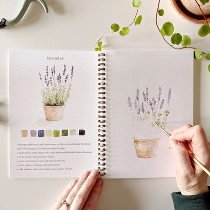 A hand paints lavender flowers in the Garden Watercolor Workbook, a spiral-bound sketchbook. Available sizes: 8x10, 9x12 inches.