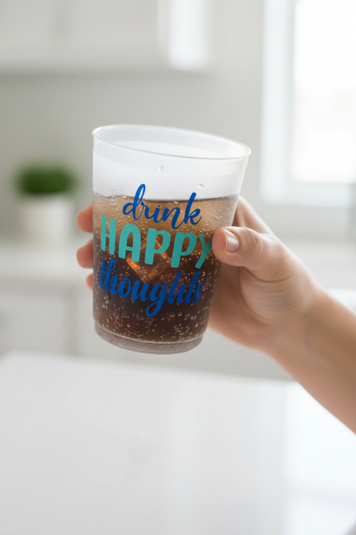 Drink Happy Thoughts Party Cup (16oz), clear with colorful text, holds a dark fizzy drink. Also available in 12oz and 20oz sizes.