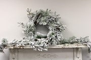 Snow-flocked evergreen wreath and snow-flocked evergreen garland with pine cones.