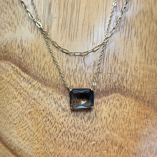 The Dula Smokey Multi-Strand Necklace features layered gold double strands and a rectangular dark gemstone pendant. Available in one adjustable size.