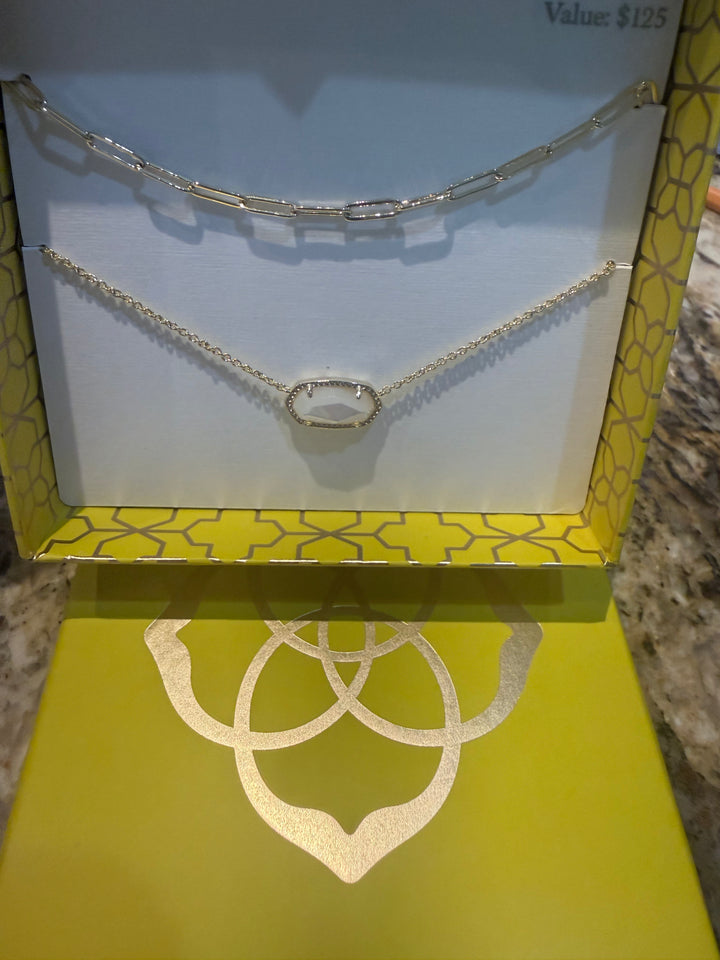 Yellow box with gold designs displaying the Elisa Courtney Necklace Gift Set Gold Ivory Mother of Pearl by Kendra Scott; includes oval link paperclip necklace and small oval pendant necklace. Size options not specified.