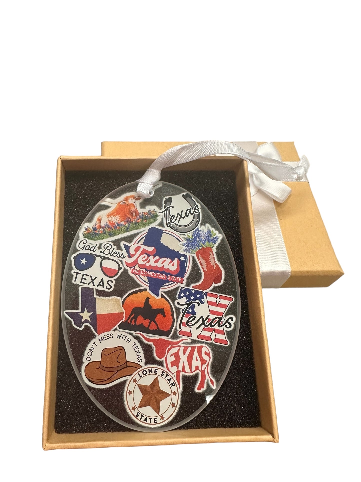 The Texas Ornament features Texas-themed stickers including a cowboy hat, the Texas flag, Longhorn cattle, a vintage car, "God Bless Texas," and "Lone Star State." Presented in an open gift box with a white ribbon. Sizes available: 3", 4".