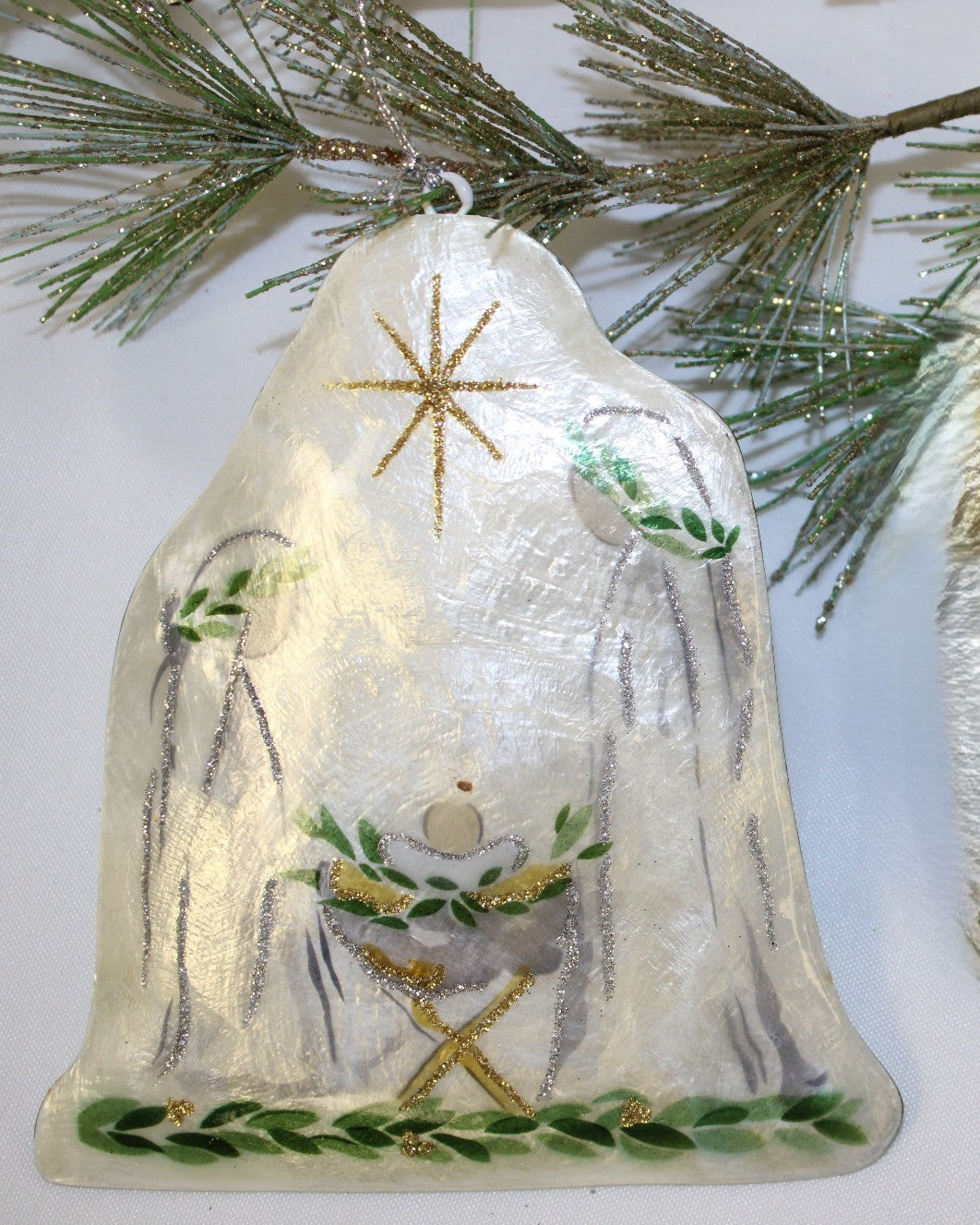 Bell-shaped Holy Family Capiz ornament with painted scene and gold glitter star.