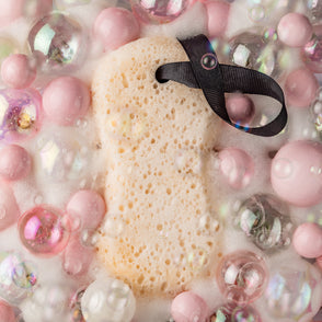 Sweet Grace Body Wash Sponge in beige with black ribbon; gently exfoliates. Available in regular and travel sizes.