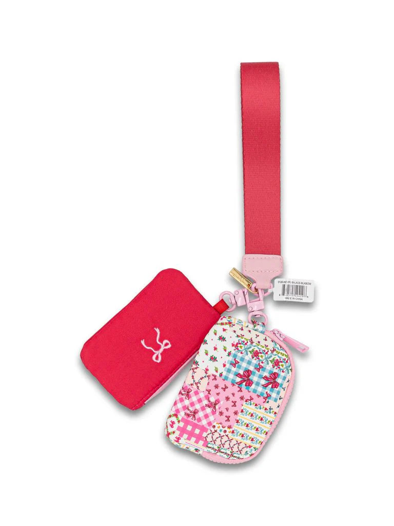 Two small quilted ID coin wristlets, one red with a white design and one in a colorful patchwork pattern, both with pink zippers and clips, attached to a wide pink strap. Sizes available: small.