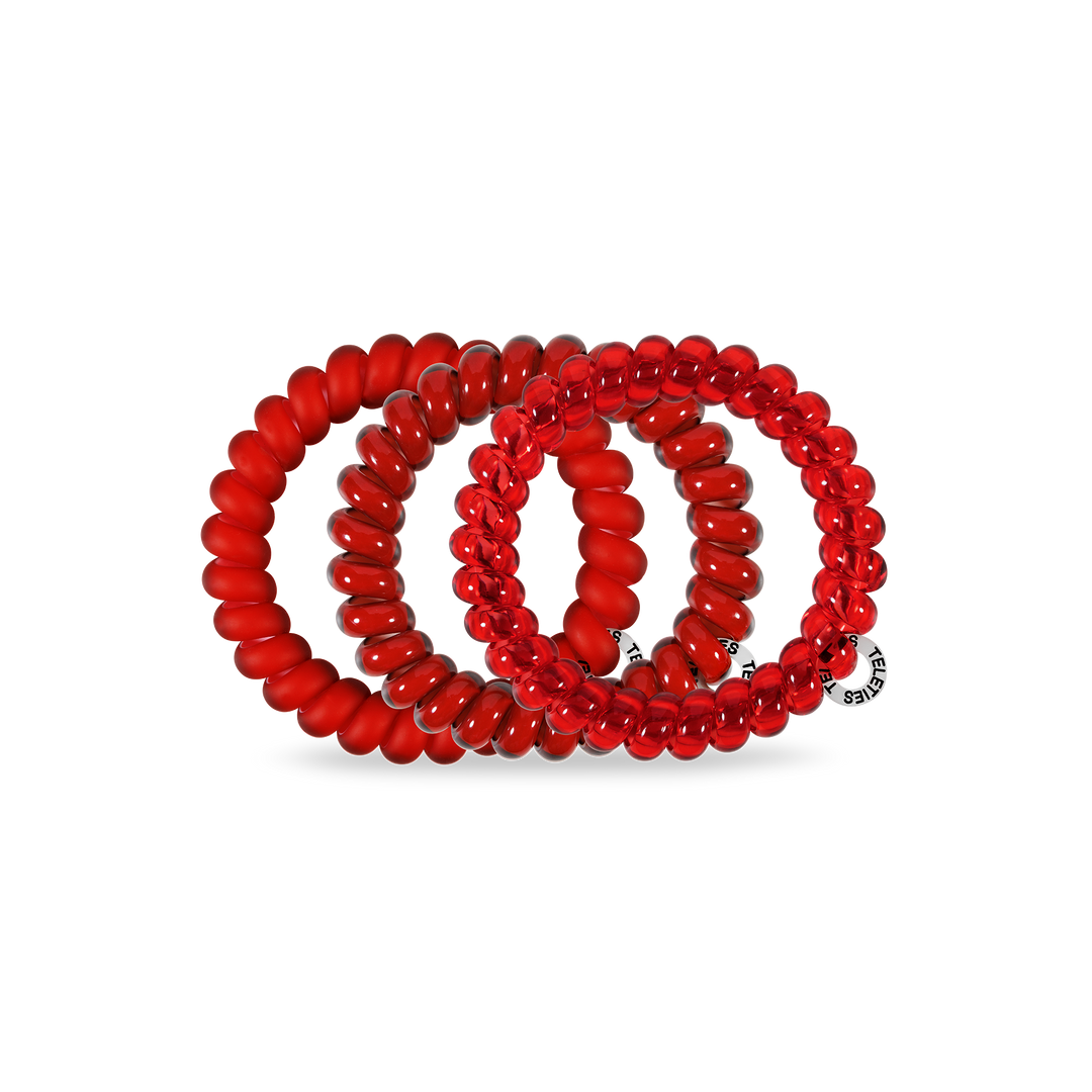 Three red Spiral Hair Coils in assorted sizes with smooth spiral design; one has a small round silver tag with text.