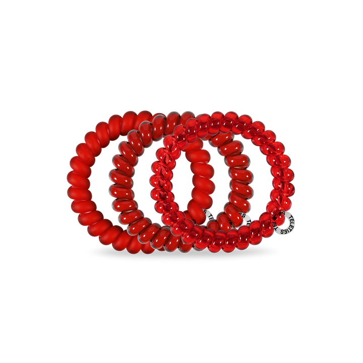Three red Spiral Hair Coils in assorted sizes with smooth spiral design; one has a small round silver tag with text.