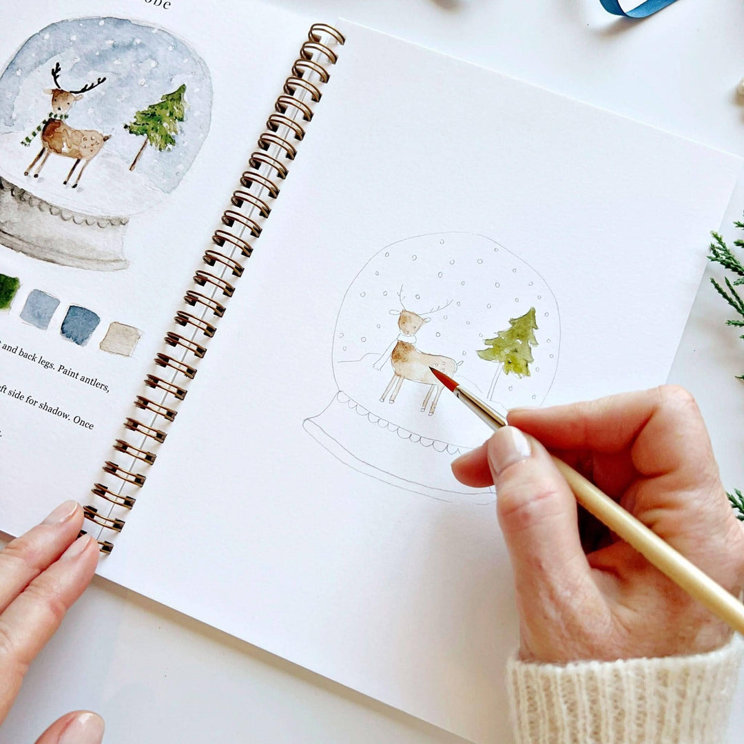 Winter watercolor workbook for painting a reindeer in a snow globe.