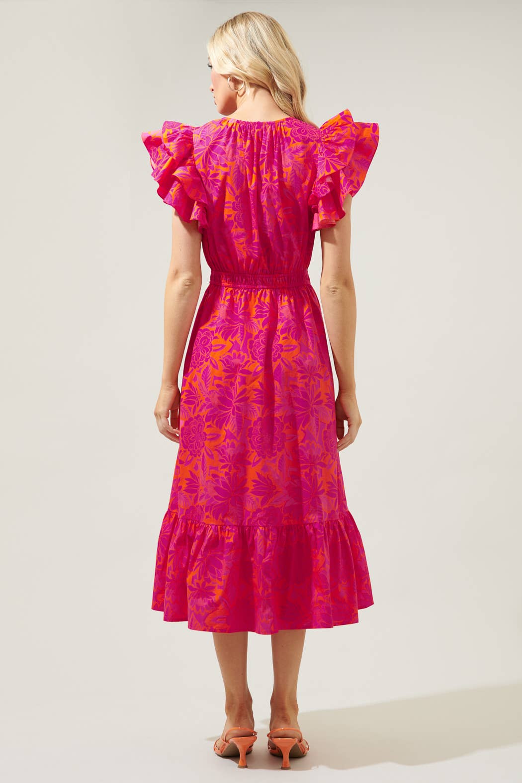 The Bali Tropics Jelina Ruffle Sleeve Midi Dress is a vibrant pink and purple piece. Features include ruffled sleeves and a tiered skirt. Available in multiple sizes.