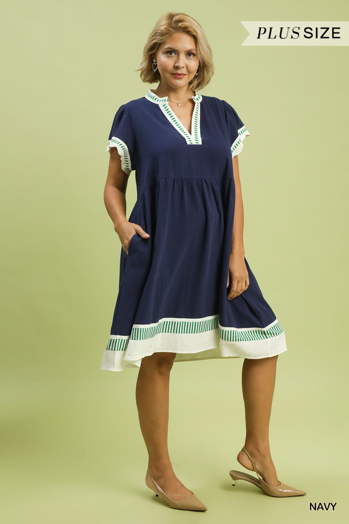 Navy Coast Linen Color Block Dress in plus sizes, featuring a navy blue tiered babydoll design with white and green trim, flutter sleeves, and pockets.