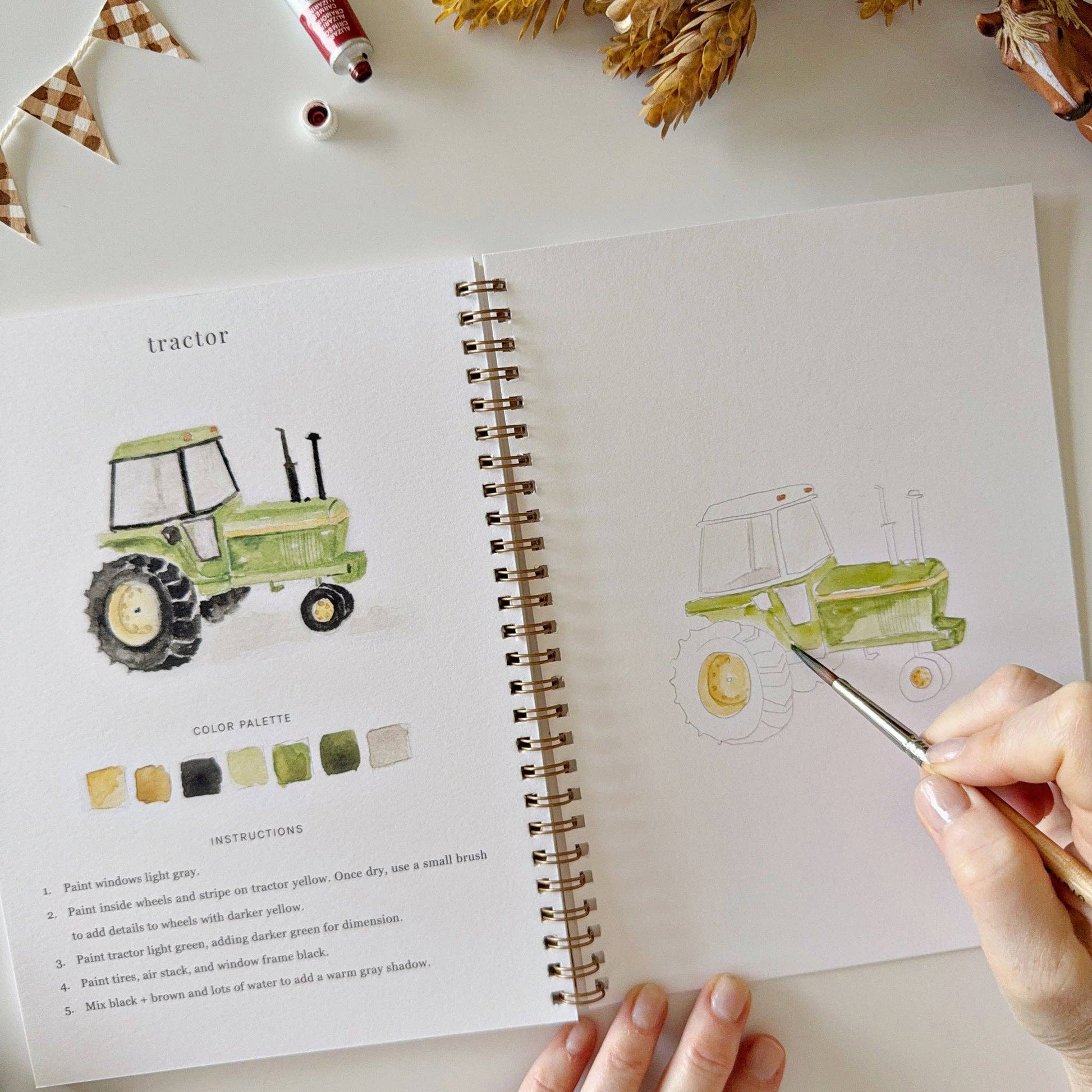 A hand paints a green tractor in the spiral-bound Farm Watercolor Workbook; includes painting instructions. Available in multiple sizes.