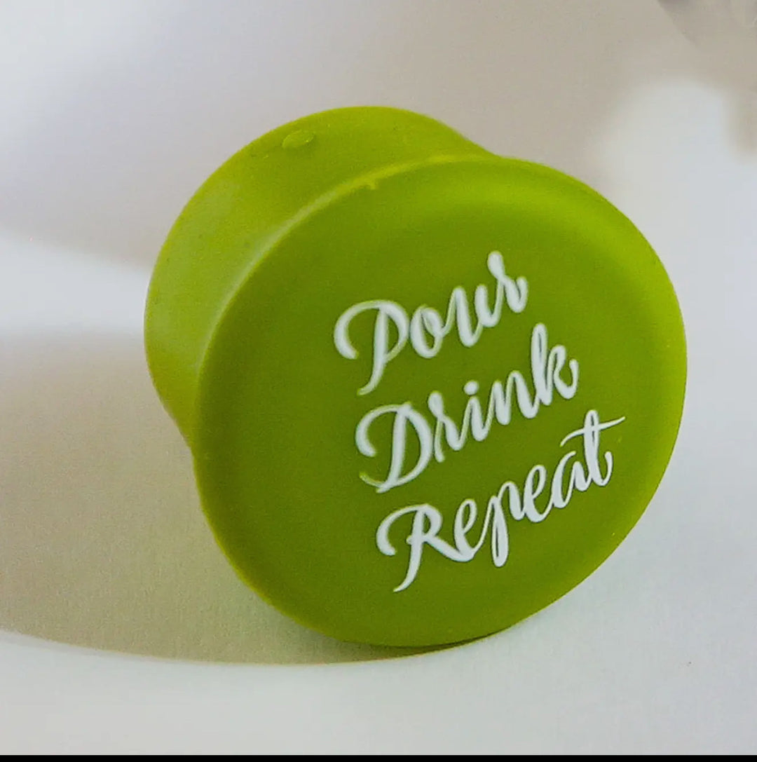 Green cap reads "Pour Drink Repeat" in white cursive; reseals wine bottles. Available in standard and large sizes.