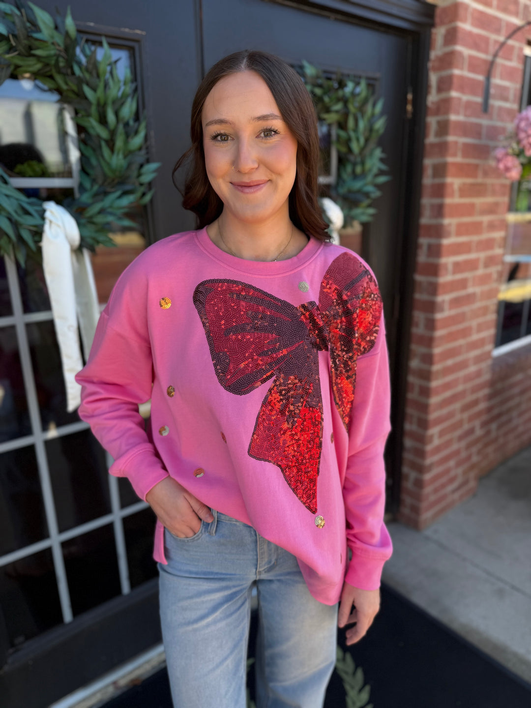 Pink sequin bow sweatshirt in a relaxed, long-sleeve cotton blend with a large, red sequined bow graphic. Sizes available: [Insert Sizes].