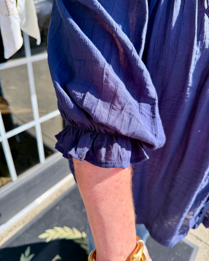 Navy Smocked Yoke Button Front Blouse in blue with crinkled textured fabric, long sleeves, and ruffled cuffs. Available in sizes XS–XL.