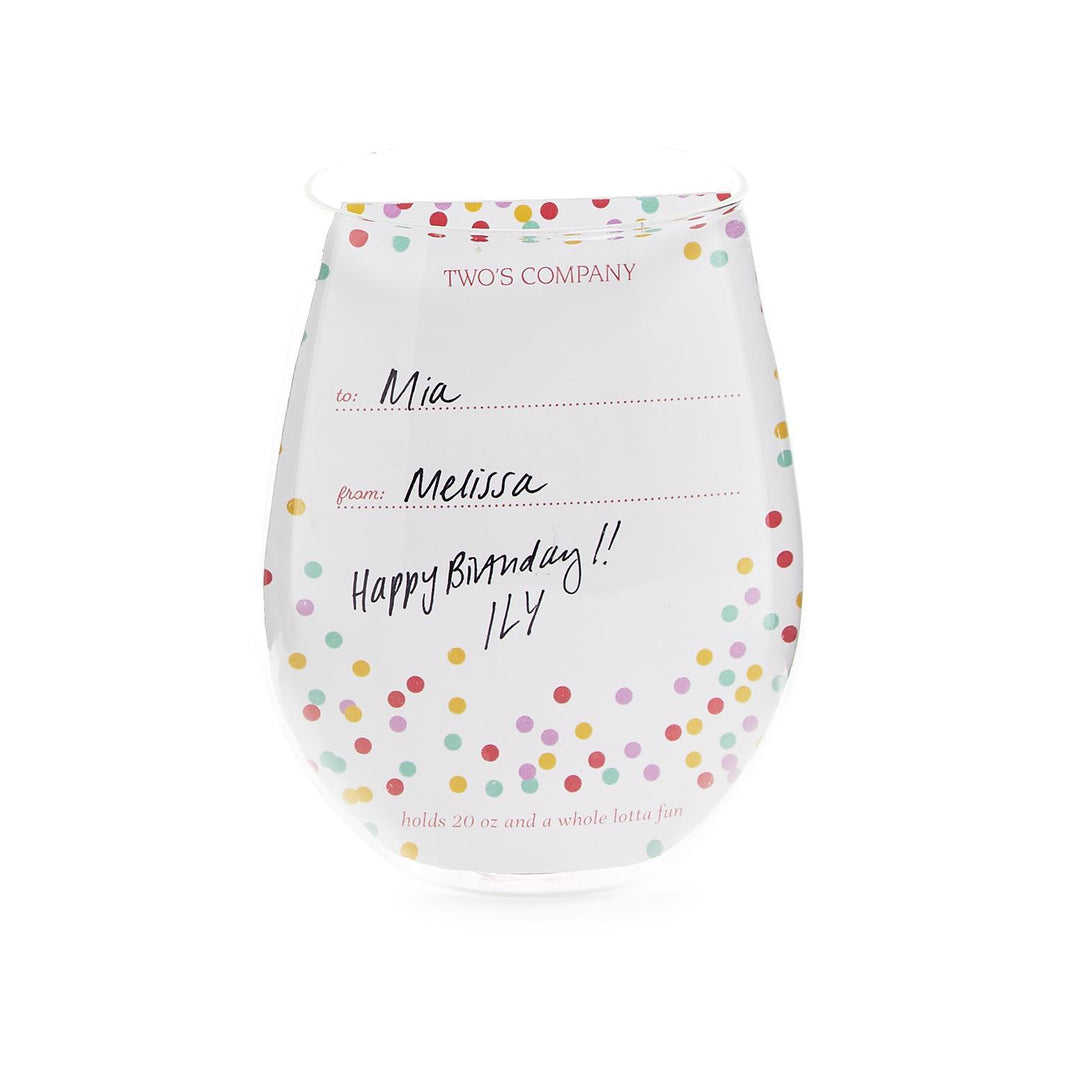 The Celebration Cake Stemless Wine Glass holds 20 oz and features colorful polka dots. The durable glass has a "to" and "from" section filled out with "Mia" and "Melissa," handwritten text saying, "Happy Birthday!! ILY," and printed text at the bottom that reads, "holds 20 oz and a whole lotta fun.
