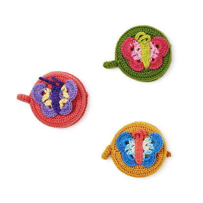 Round hand-crocheted measuring tape with butterfly designs in pink-green, purple-red, or blue-yellow. Size: 2.4" diameter.