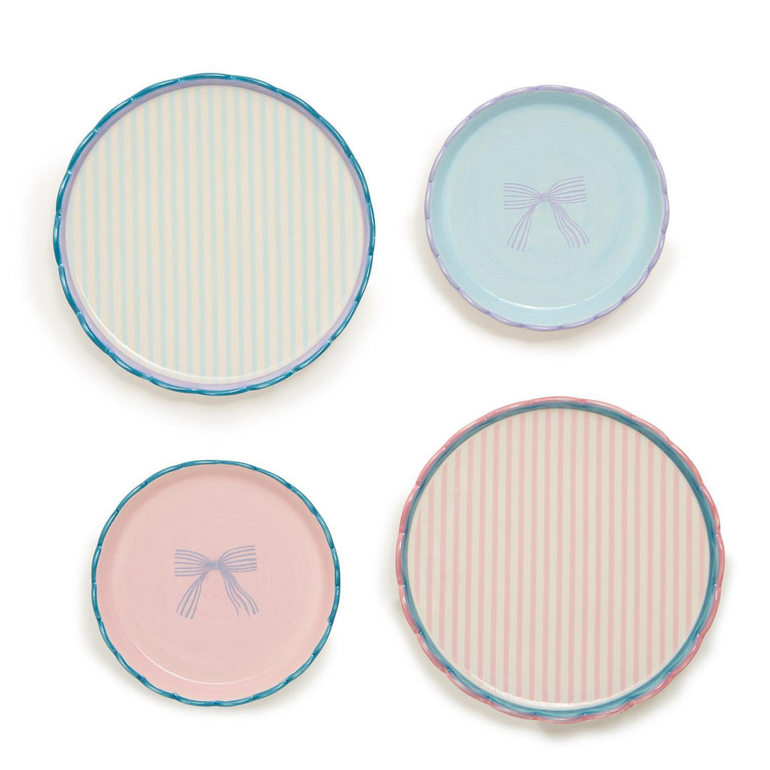 The "Beautiful Bow Set of 2 Scallop Edge Trinket Dishes" consists of four round stoneware plates: two with pale pink stripes and blue and green rims, and two with light blue and teal designs featuring central bow illustrations. Sizes available: not specified.