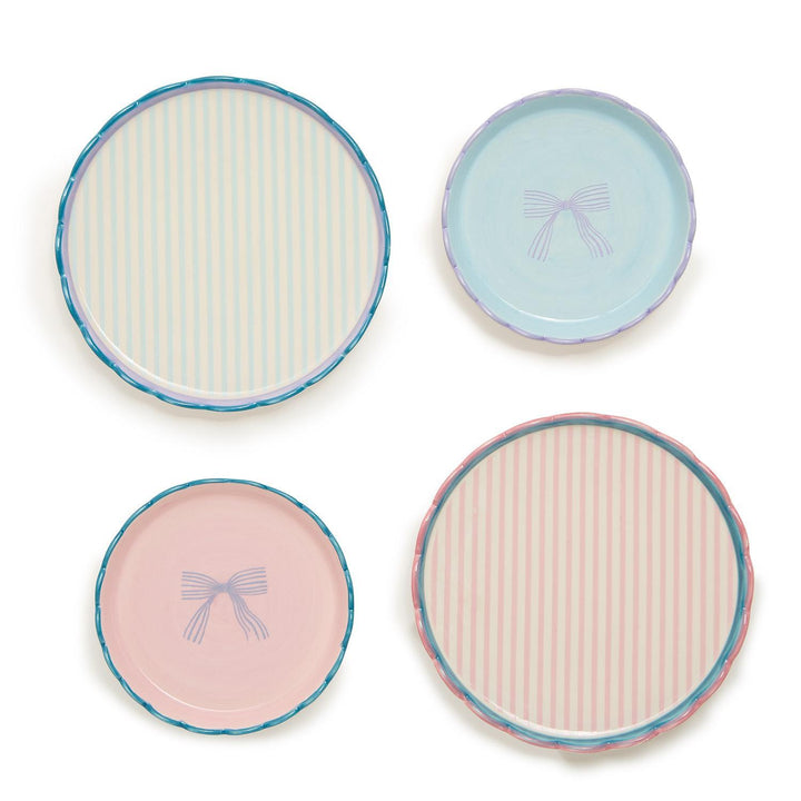 The "Beautiful Bow Set of 2 Scallop Edge Trinket Dishes" consists of four round stoneware plates: two with pale pink stripes and blue and green rims, and two with light blue and teal designs featuring central bow illustrations. Sizes available: not specified.
