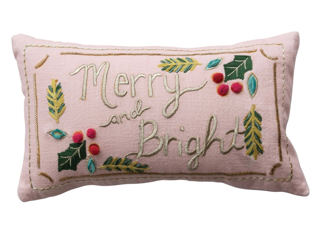 Merry and Bright lumbar pillow, a rectangular light pink cushion embroidered with “Merry and Bright” surrounded by holly, berries, and pine sprigs.