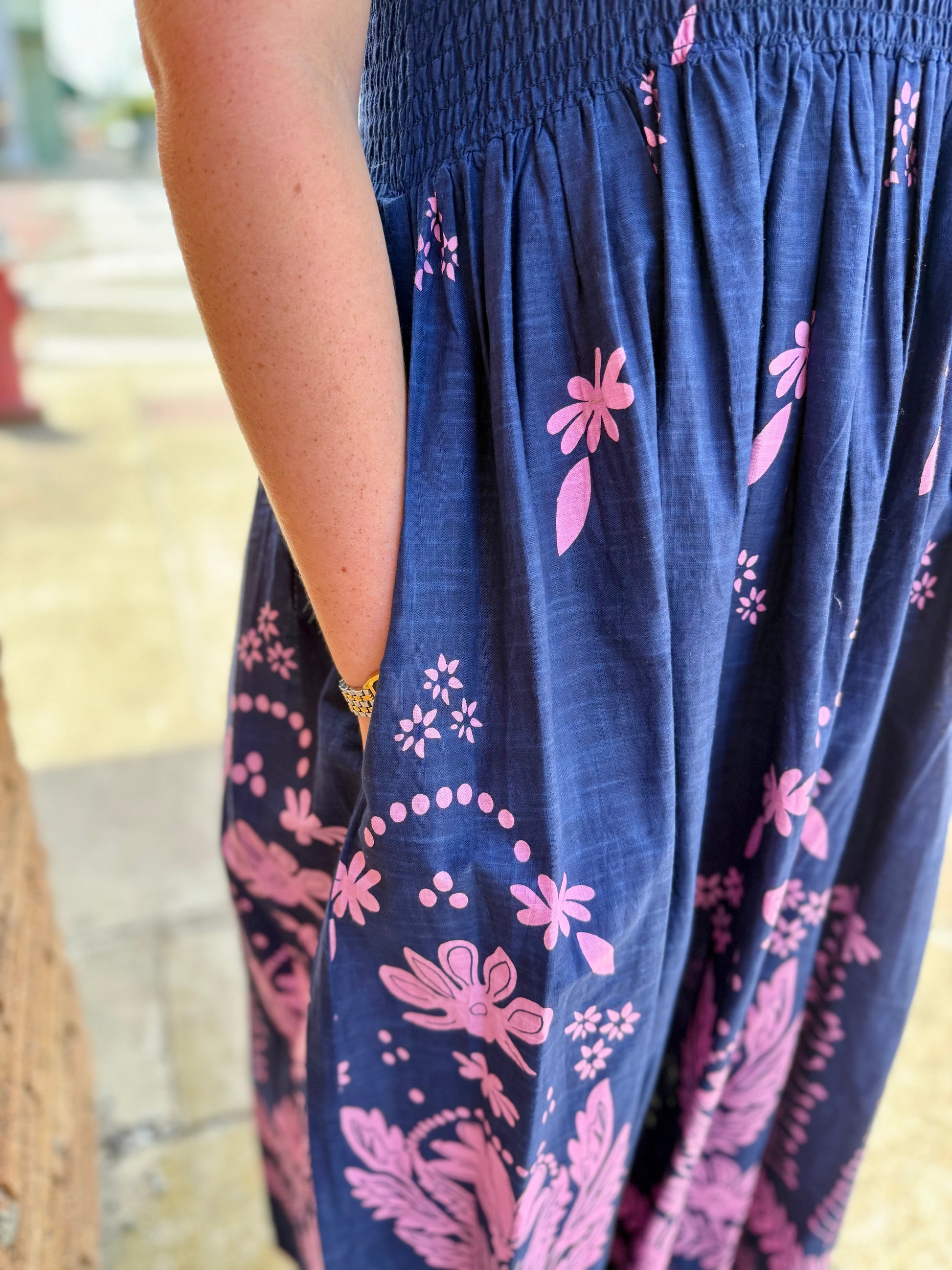 Navy Smocked Border Dress with pink floral patterns, gathered waist, and side pockets. Available in sizes XS-XL.