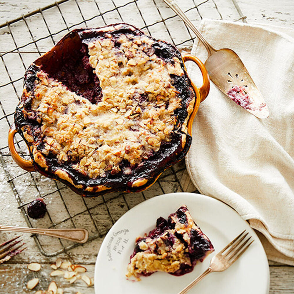 Baked berry crumble pie with a missing slice on wire rack; available in whole pie and individual slices.