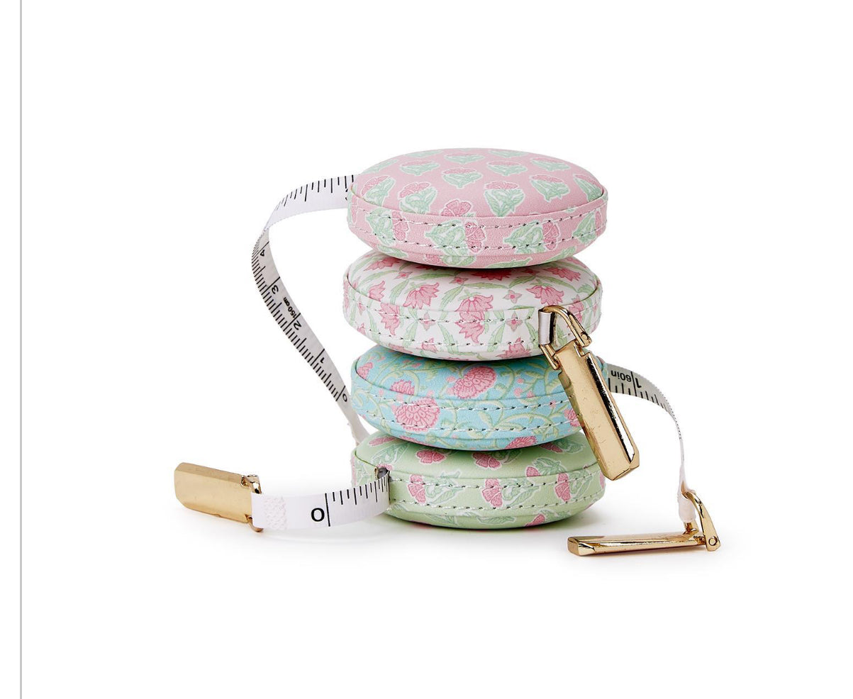 Floral Block Print Measuring Tapes: Four round, pastel-colored tape measures with unique floral, heart, and cactus designs. Gold-toned clips at the end. Size: standard tape measure length.