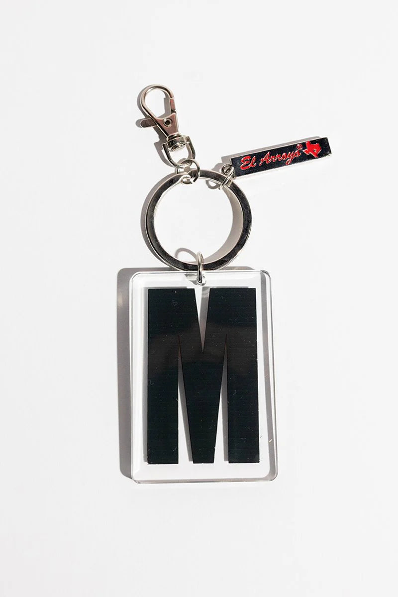 Clear acrylic keychain with bold black "M", small metal tag engraved "El Arroyo" and outlined red Texas. Size: one size.